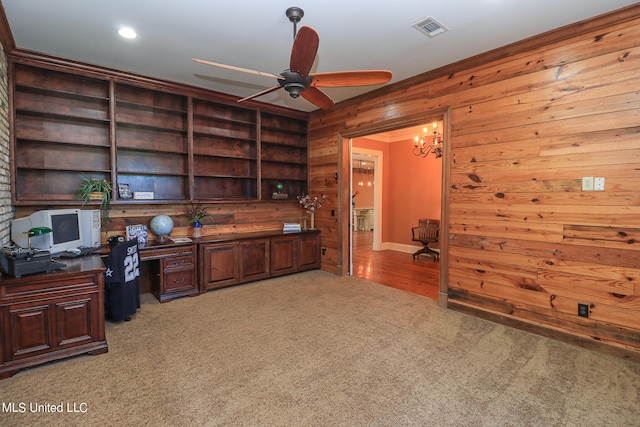 carpeted home office featuring built in desk, ceiling fan with notable chandelier, and wooden walls