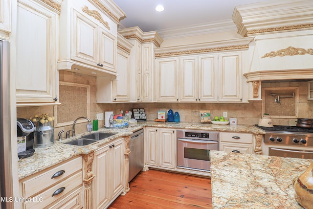 kitchen with light stone counters, light hardwood / wood-style flooring, ornamental molding, sink, and stainless steel appliances