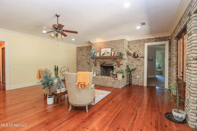 living room featuring brick wall, ornamental molding, a brick fireplace, and hardwood / wood-style flooring