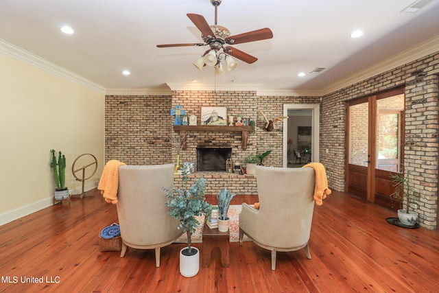 living room featuring hardwood / wood-style flooring, brick wall, ornamental molding, a brick fireplace, and ceiling fan