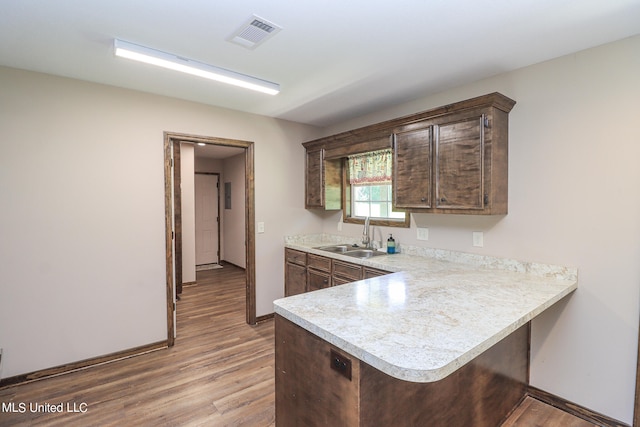 kitchen featuring sink, kitchen peninsula, dark brown cabinets, and light wood-type flooring