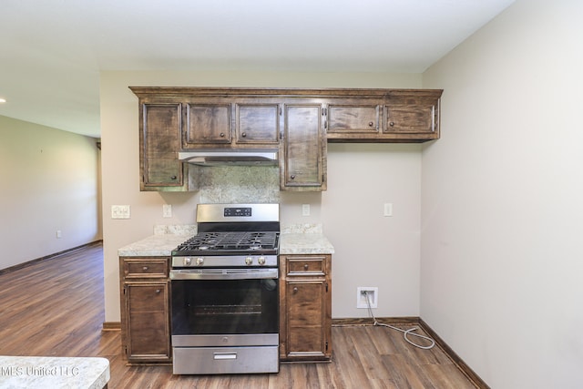 kitchen featuring dark brown cabinets, stainless steel gas range oven, exhaust hood, and dark hardwood / wood-style flooring