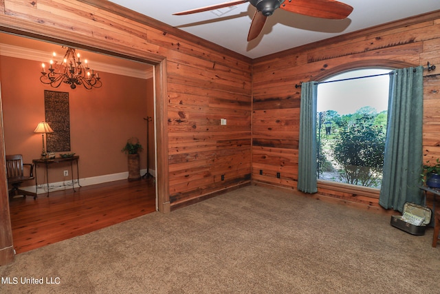 spare room featuring ornamental molding, dark hardwood / wood-style flooring, wooden walls, and ceiling fan with notable chandelier