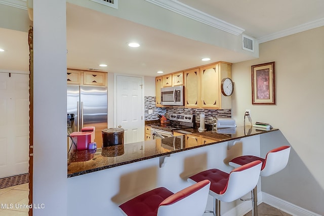 kitchen with appliances with stainless steel finishes, crown molding, backsplash, dark stone countertops, and light tile patterned floors