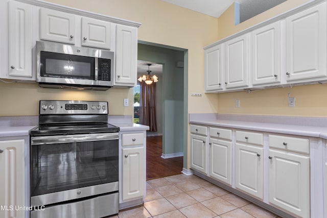 kitchen with light tile patterned flooring, stainless steel appliances, pendant lighting, white cabinets, and a notable chandelier