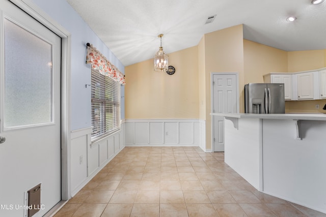 kitchen with lofted ceiling, stainless steel fridge, white cabinets, hanging light fixtures, and a kitchen breakfast bar