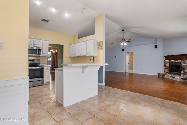 kitchen featuring lofted ceiling, appliances with stainless steel finishes, a breakfast bar, white cabinetry, and light hardwood / wood-style flooring