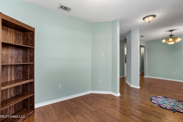 spare room featuring a notable chandelier, a textured ceiling, and dark wood-type flooring