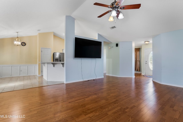 unfurnished living room with light hardwood / wood-style floors, ceiling fan with notable chandelier, and vaulted ceiling