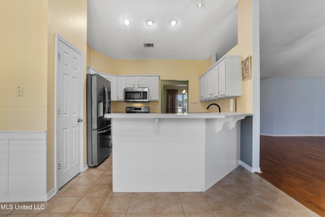 kitchen featuring a breakfast bar area, light hardwood / wood-style flooring, kitchen peninsula, white cabinetry, and appliances with stainless steel finishes