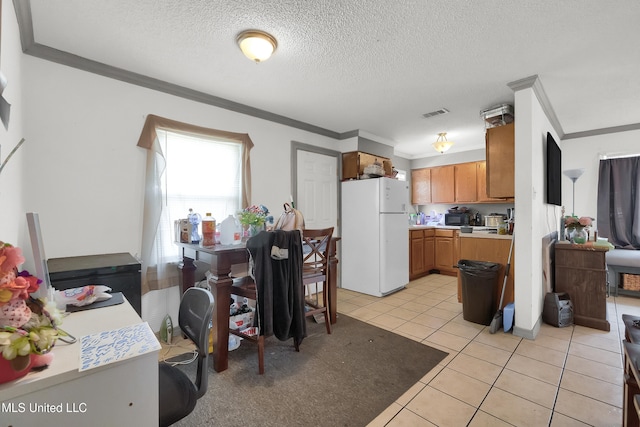 kitchen featuring a textured ceiling, light tile patterned floors, white fridge, and crown molding