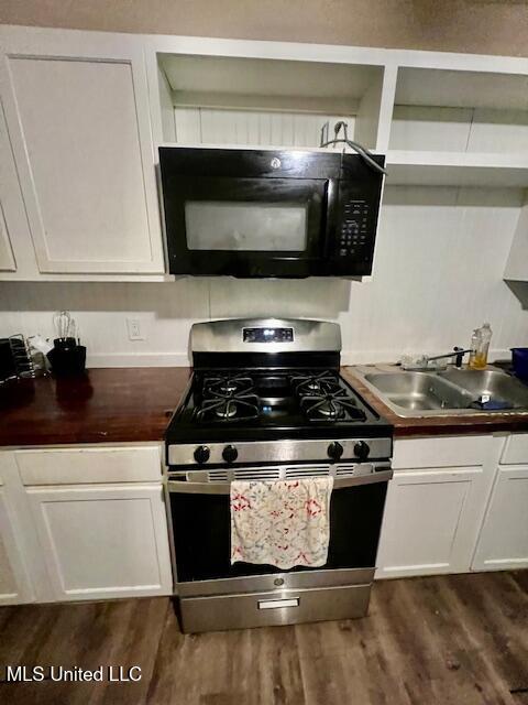kitchen featuring white cabinets, stainless steel gas stove, a sink, black microwave, and dark wood-style flooring