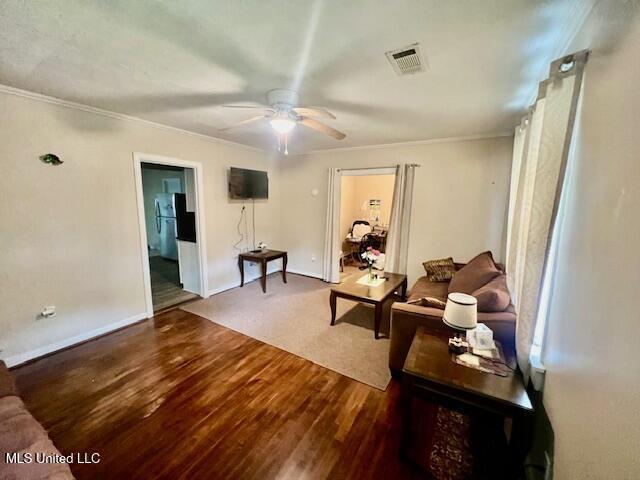 living area with ceiling fan, ornamental molding, wood finished floors, and visible vents