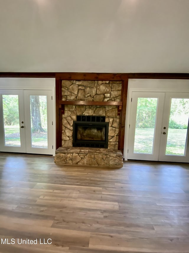 unfurnished living room with a stone fireplace, french doors, and wood finished floors