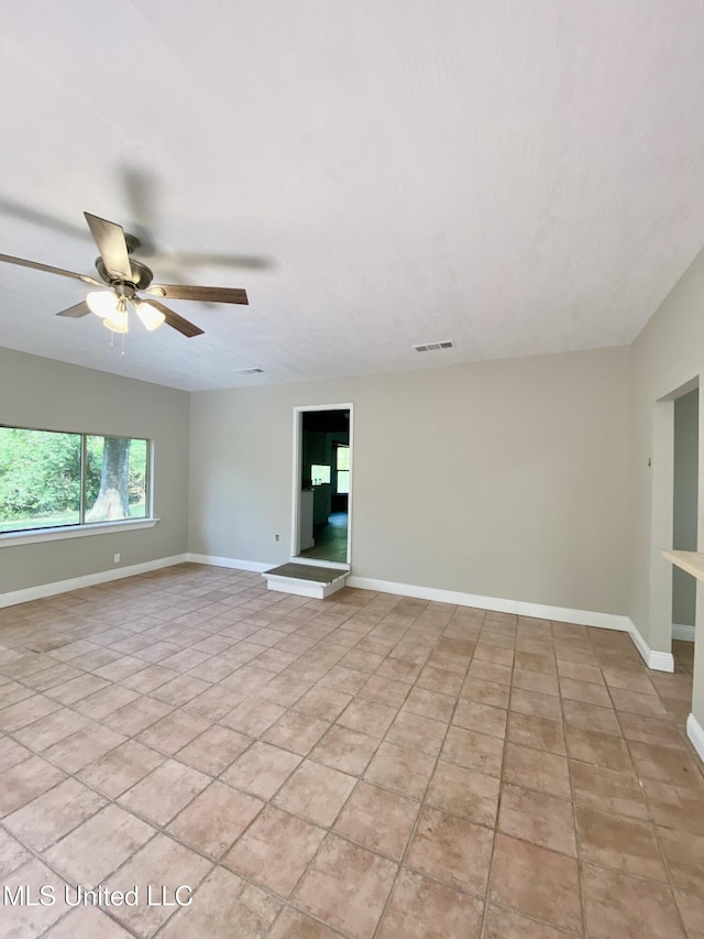 empty room with baseboards, ceiling fan, light tile patterned floors, and visible vents