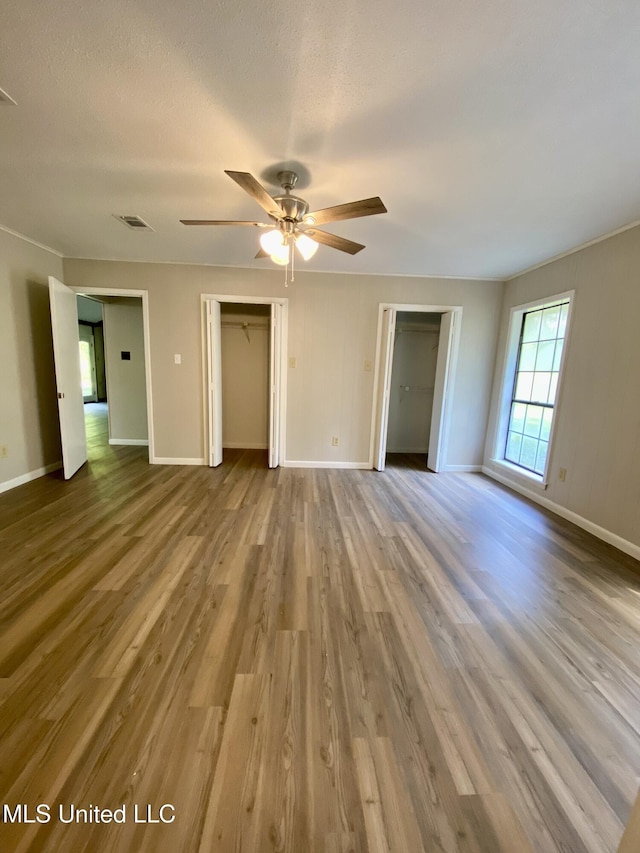 unfurnished bedroom featuring baseboards, two closets, and wood finished floors