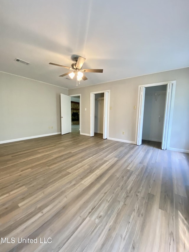 unfurnished bedroom featuring visible vents, a fireplace, wood finished floors, baseboards, and multiple closets