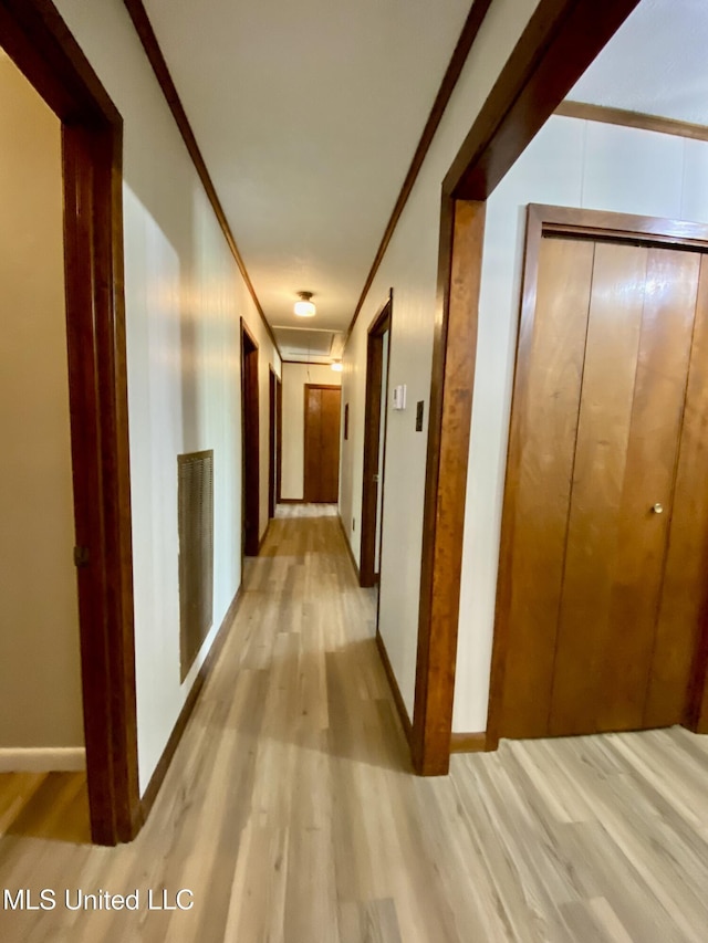 hall featuring light wood-style floors, ornamental molding, and baseboards