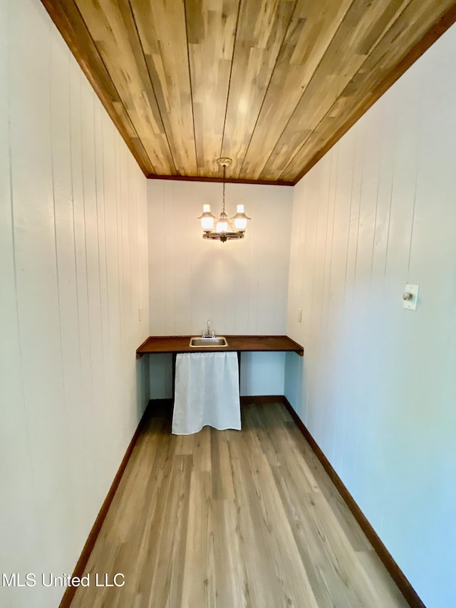 unfurnished dining area with wood finished floors, a sink, wooden ceiling, baseboards, and a notable chandelier