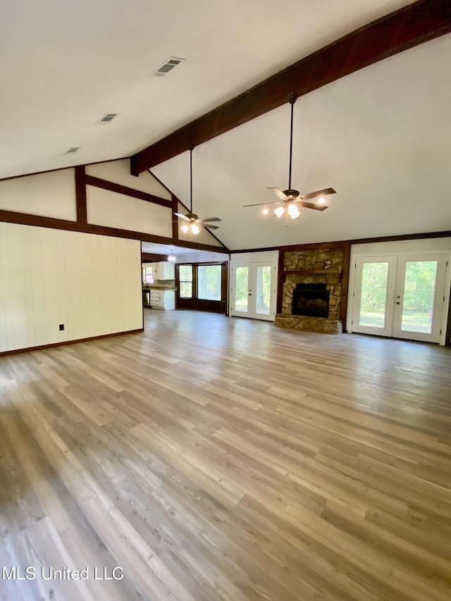 unfurnished living room featuring lofted ceiling with beams, french doors, a stone fireplace, and a wealth of natural light