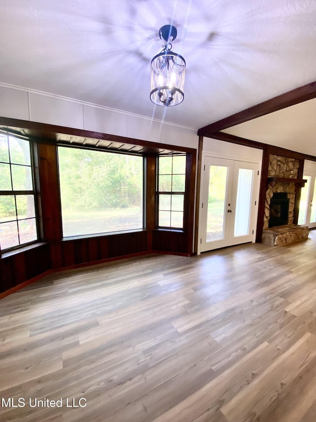 unfurnished living room featuring a stone fireplace, ornamental molding, wood finished floors, and a notable chandelier