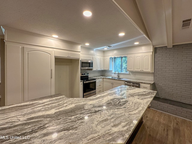 kitchen featuring white cabinets, appliances with stainless steel finishes, dark hardwood / wood-style floors, light stone counters, and brick wall