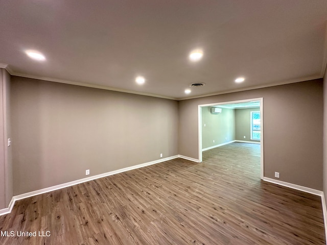 empty room featuring a wall unit AC, crown molding, and wood-type flooring