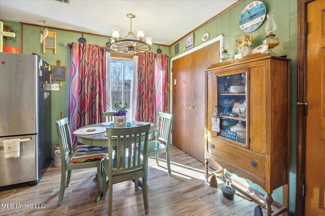 dining area featuring a textured ceiling, wood-type flooring, a chandelier, ornamental molding, and wood walls