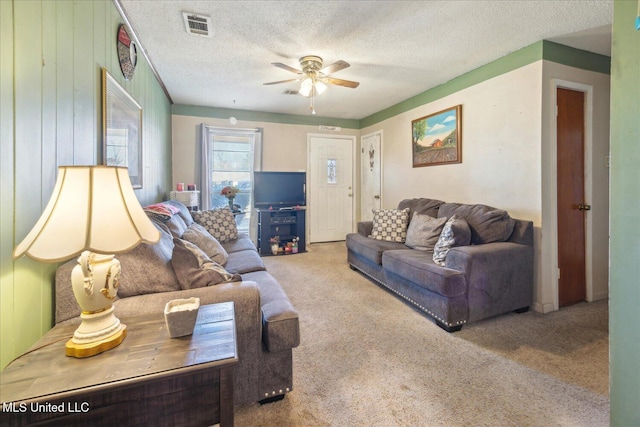 living room featuring ceiling fan, a textured ceiling, wooden walls, and carpet flooring