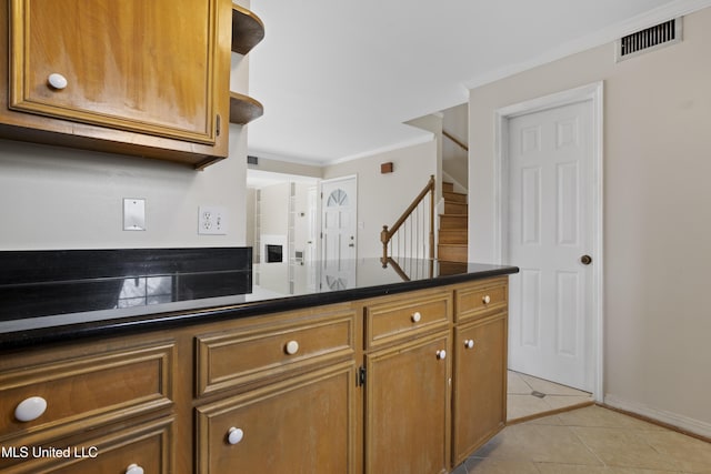 kitchen featuring light tile patterned floors, brown cabinetry, visible vents, crown molding, and dark countertops