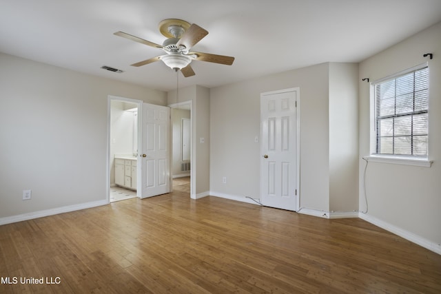 unfurnished bedroom featuring visible vents, baseboards, ensuite bath, and wood finished floors