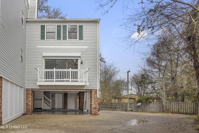 view of front facade featuring brick siding, a balcony, driveway, and fence