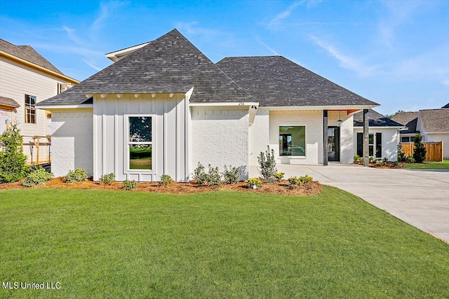 view of front of property featuring board and batten siding, a front yard, concrete driveway, and a shingled roof