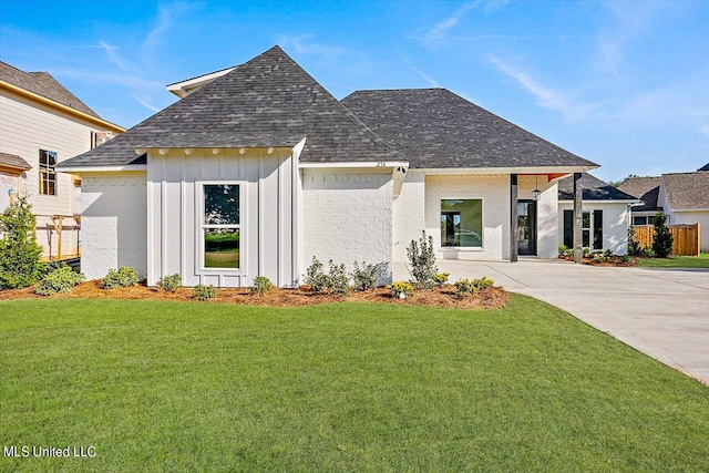 view of front of home with fence, a shingled roof, a front lawn, concrete driveway, and board and batten siding