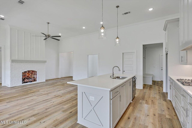 kitchen with light wood-style floors, appliances with stainless steel finishes, light countertops, a brick fireplace, and a sink