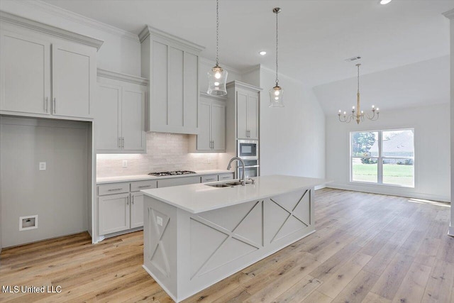 kitchen featuring an island with sink, sink, pendant lighting, light wood-type flooring, and appliances with stainless steel finishes