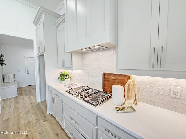 kitchen featuring light wood finished floors, stainless steel gas cooktop, custom exhaust hood, backsplash, and ornamental molding