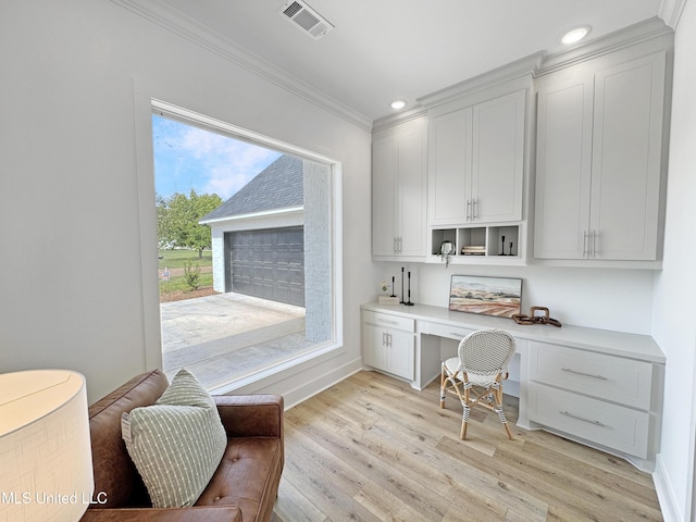 office space featuring light wood finished floors, baseboards, visible vents, built in desk, and crown molding