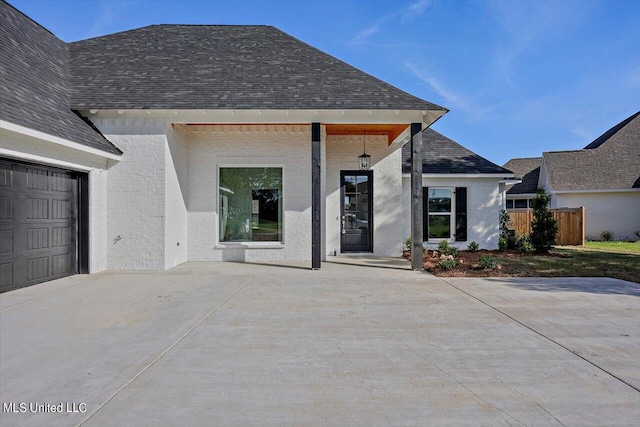view of front of house featuring an attached garage, a shingled roof, driveway, and fence