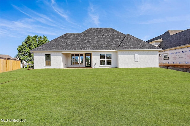 back of house featuring roof with shingles, a lawn, and fence