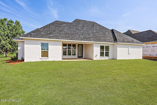 rear view of house featuring a shingled roof, a lawn, and stucco siding