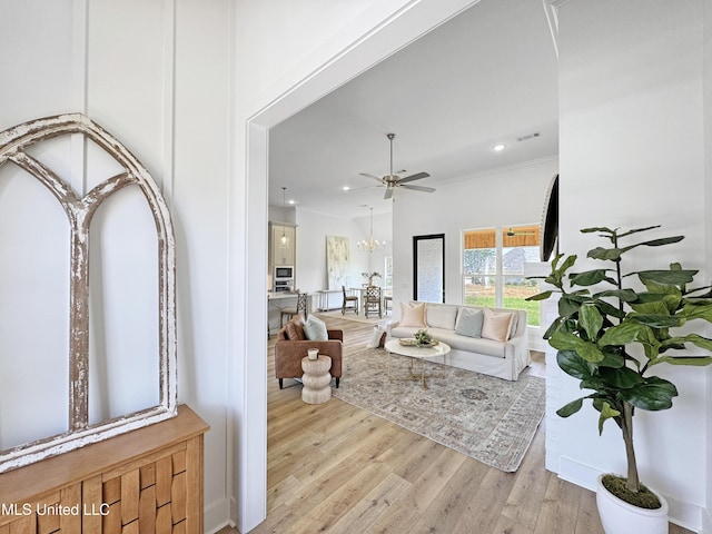 living area with light wood-type flooring, visible vents, recessed lighting, ceiling fan with notable chandelier, and ornamental molding