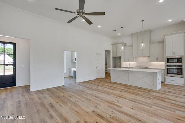 kitchen with pendant lighting, appliances with stainless steel finishes, light hardwood / wood-style flooring, and a kitchen island with sink