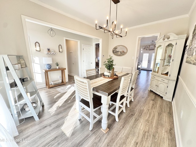 dining area featuring light wood-type flooring, french doors, crown molding, and a chandelier