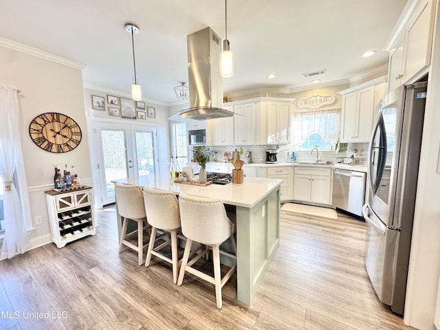 kitchen with stainless steel appliances, decorative light fixtures, a center island, white cabinets, and island range hood