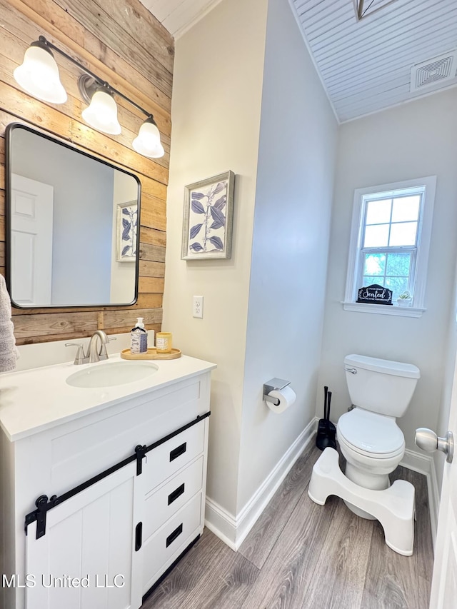 bathroom featuring wood-type flooring, wooden walls, vanity, and toilet