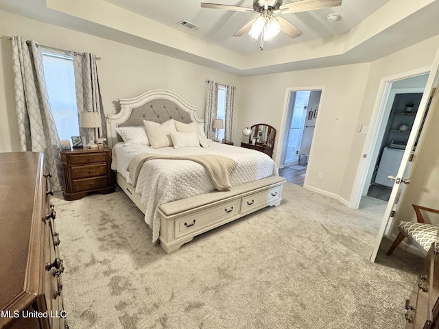 bedroom featuring a raised ceiling, ceiling fan, light carpet, and connected bathroom