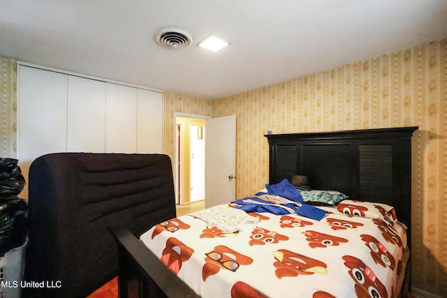 bedroom with wallpapered walls, visible vents, and a closet