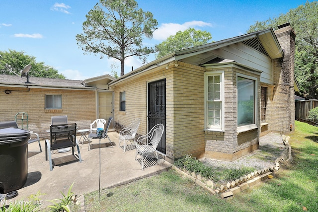 rear view of house with brick siding, a patio area, and a chimney