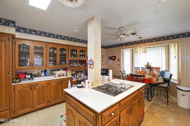 kitchen with brown cabinets, light countertops, stainless steel electric cooktop, wallpapered walls, and glass insert cabinets